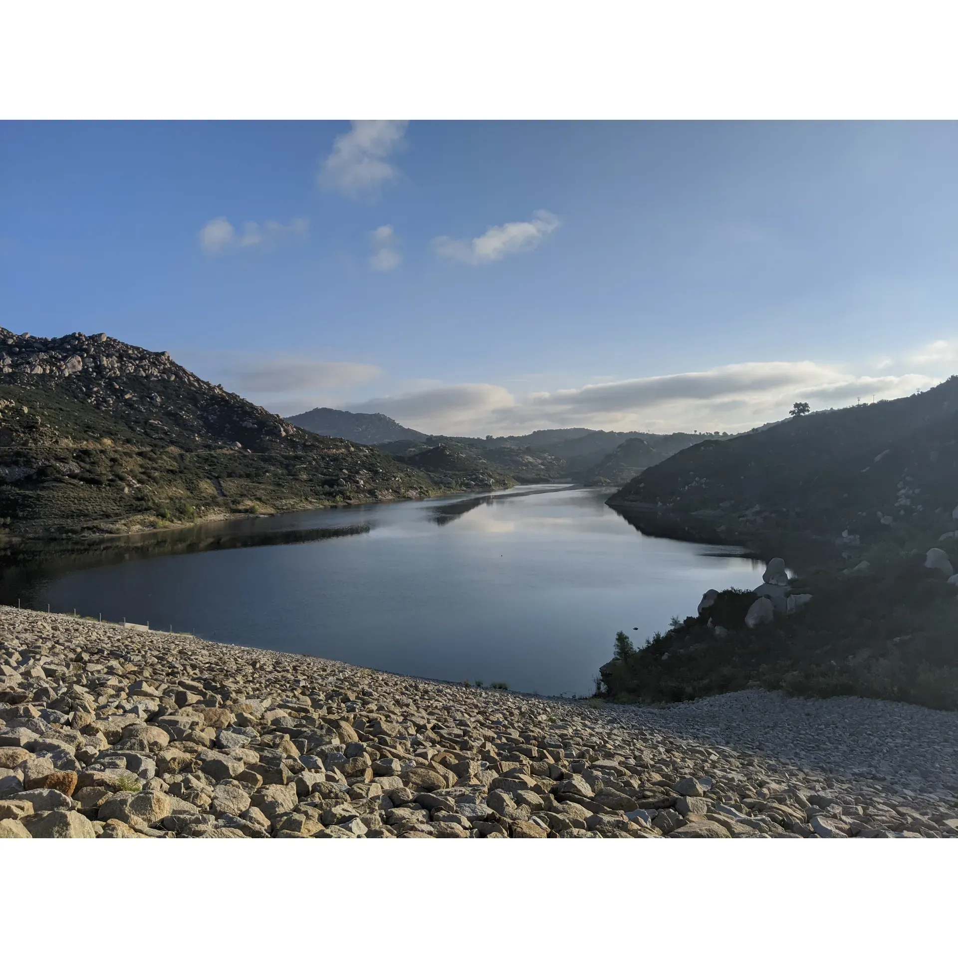 Lake Ramona offers an invigorating outdoor experience for those seeking adventure and tranquility in the heart of nature. Beginning from the Blue Sky Ecological Reserve parking lot in Poway, visitors embark on a rewarding 2.5-mile journey embraced by the beauty of the environment. The consistently wide trail doubles as an access road, ensuring a well-maintained path for hikers.

As adventurers make their way to the lake, they encounter a moderately steep incline in the latter half of the trek, a perfect challenge for those looking to test their stamina. Along the route, convenient porta potties provide basic amenities for traveler comfort. Hikers are advised to bring plenty of water and snacks to stay energized, as no additional services are available on-site.

Upon arrival, the breathtaking beauty of Lake Ramona itself is the ultimate prize. This pristine lake, embraced by its natural surroundings, offers a peaceful retreat away from crowds, allowing visitors a sense of isolation and serenity. Early risers are rewarded with cooler temperatures and a more comfortable hike.

For enthusiasts of the sport, the lake is acclaimed for its exceptional bass fishing opportunities. The clear, still waters require finesse and stealth, with success often found near the tules and by the dam. Fishermen praise the quality of the catch, with fluorocarbon lines recommended for the best results. While swimming is not permitted, the thrill of the catch and release is a memorable experience for all who cast their line.

With a trek that takes roughly 40 minutes to an hour one way, Lake Ramona is a gorgeous destination for spending a day surrounded by the beauty of the outdoors, whether through a challenging hike or a peaceful day of fishing. The return journey is noted to be easier, providing a satisfying conclusion to an awe-inspiring adventure in the great outdoors. Description by ChatGPT.