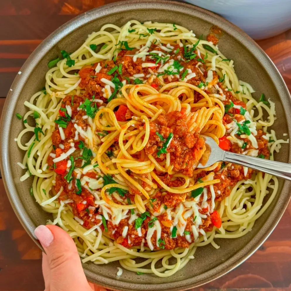 A hearty and comforting spaghetti dish featuring a rich meat sauce made with ground beef, vegetables, and Mama's Marinara sauce, topped with melted mozzarella cheese and fresh parsley.