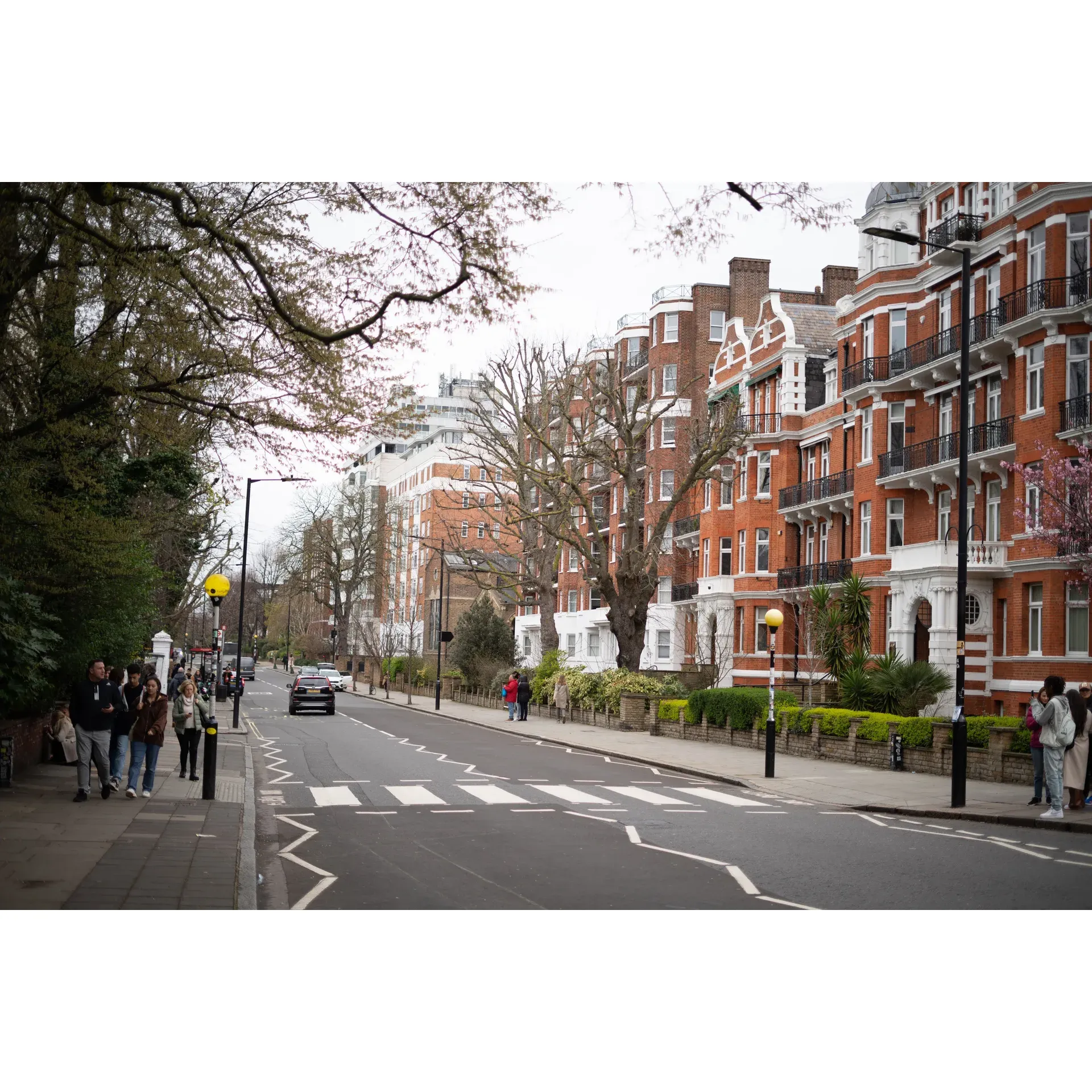 Step into the shoes of music history at Abbey Road, an undeniably iconic street that pulses with the footsteps of countless Beatles enthusiasts and tourists alike, all seeking to recreate the famous album cover. This storied thoroughfare offers an inviting and friendly atmosphere, where the spirit of the 'Fab Four' still echoes with every step taken on the celebrated pedestrian crossing. With visitors from around the world flocking to this site, you'll find a sense of camaraderie and excitement in the air. 

Take your place on the zebra crossing and strike a pose, as the local traffic graciously pauses, allowing fans to capture their moment without haste. Photographers find delight in the patient and understanding nature of passing drivers, which speaks volumes about the respect for the cultural significance of this landmark. 

For Beatles aficionados, Abbey Road is more than just a crossing or a stretch of asphalt—it's a pilgrimage destination. Whether you're there to follow in the footsteps of a loved one's musical heroes or to embrace your own passion for the legendary band, the experience is enveloped in a reverent and joyful ambiance. 

Even those who stumble upon Abbey Road out of mere curiosity can't help but get swept up in its charm. The street lives up to its fame with an energetic yet orderly scene, as people from all walks of life come together, unified by the desire to capture a piece of music history. To avoid the crowd and allow the magic of the place to truly sink in, consider visiting during the quieter moments of dawn. Regardless of the time you choose to go, Abbey Road invites you to be part of a living legacy that continues to inspire and bring joy to fans across the globe. Description by ChatGPT.