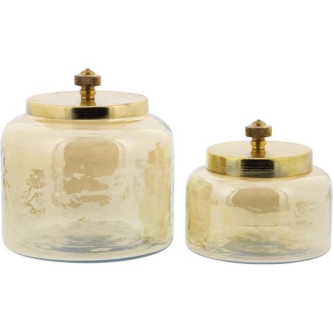 The CosmoLiving by Cosmopolitan Glass Decorative Jars with Metal Lids, Set of 2, are a stylish and modern addition to any room in your home. The set includes two jars, one measuring 4 inches in height and the other 5 inches, both featuring a sleek gold finish.