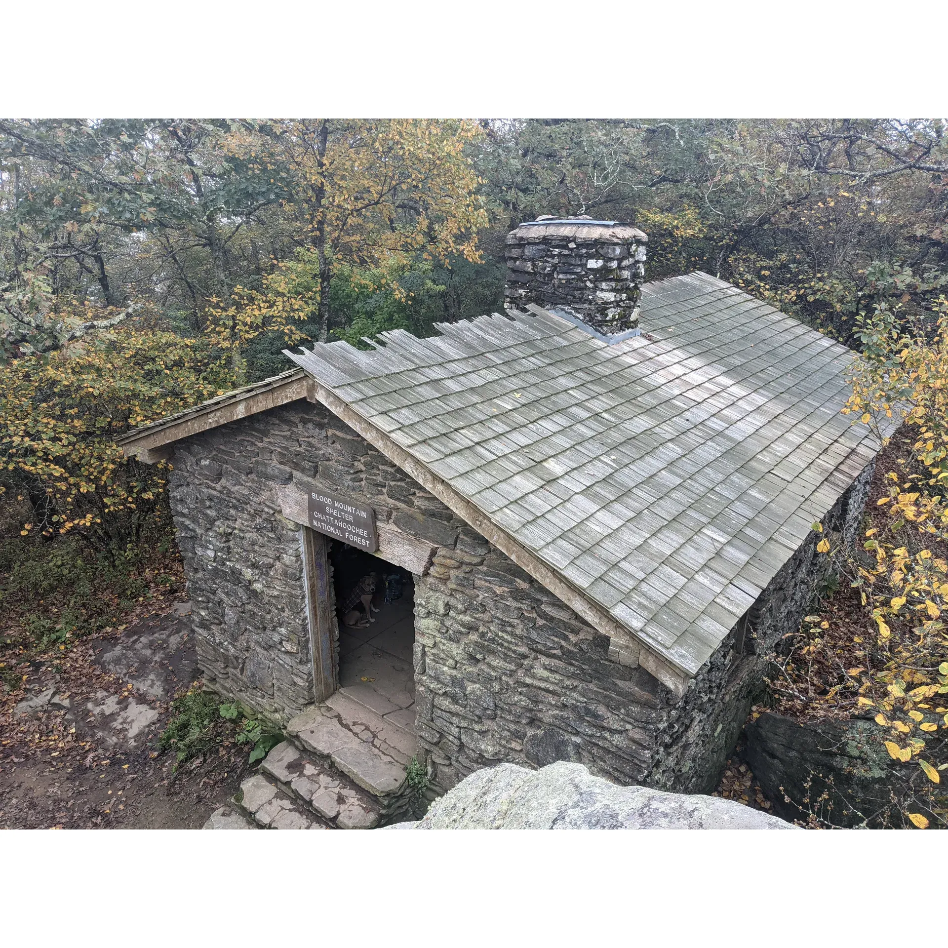 Blood Mountain Shelter stands as a historic haven for hikers traversing the scenic Appalachian Trail. Constructed in 1934 by the industrious Civilian Conservation Corps, the shelter presents an architecturally stunning edifice crafted from hand-hewn stone that blends beautifully with the rugged mountain surroundings. Visitors often regard it as an architectural gem, offering a unique blend of history and utility on their journey through the wilderness.

For those in search of serenity and awe-inspiring vistas, the shelter vicinity does not disappoint. A nearby privy offers what many have called the most majestic views in Georgia, allowing one to commune with nature in a setting that's both tranquil and breathtaking. The shelter's proximate rocky outcroppings serve as an unparalleled perch from which to observe the grandeur of the landscape, making it the perfect spot for witnessing the splendor of both sunset and sunrise.

The trek to Blood Mountain Shelter is an invigorating adventure, complete with the challenge of impressive elevation gains and an undulating terrain that rewards every step with a sense of accomplishment. Hikers are encouraged to bring ample water to stay hydrated and perhaps a snack to refuel, as the journey, while entirely rewarding, is a true testament to the tenacity of the spirited outdoorsperson. The experience is further enriched by the camaraderie of fellow travelers and the shared joy of reaching the summit together.

Visitors who choose to spend time at the shelter can expect to bond over tales of the day's climb and relax among the open areas dotting the mountain top. These spots offer idyllic settings for rest and reflection, accompanied by panoramic views of the surrounding mountains that serve as a perfect backdrop for a tranquil picnic or quiet contemplation.

Blood Mountain Shelter, with its rich history, stunning architecture, and sublime natural setting, is a testament to the timeless allure of the Appalachian wilderness. It promises an unforgettable experience, welcoming hikers from all walks of life to find solace and grandeur atop one of Georgia's most cherished peaks. Description by ChatGPT.